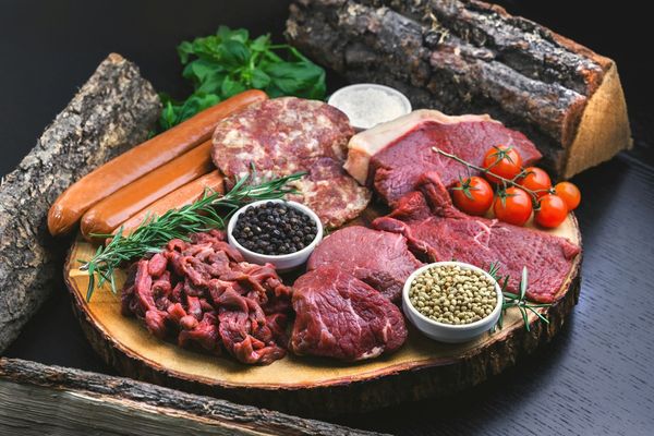 Carnes cruas, linguiças e temperos em uma tábua de madeira